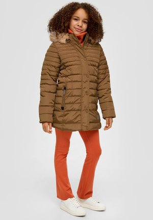 Braune Pufferjacke mit einem mit Fell gefütterten Kapuze, verfügt über eine Reißverschlusstasche und Knopfverschlüsse. Getragen über orangenen Hosen und weißen Turnschuhen.