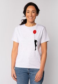T-shirt en coton blanc avec une silhouette noire d'un enfant tenant un ballon rouge, à manches courtes et col rond.