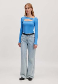 Blauw langemouwen top met een uitsnijding, gecombineerd met lichtgewassen wijde jeans en een zwarte riem. Glad materiaal en casual ontwerp.