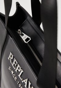 Svart skinn tote med glidelås, sølvfarget hardware og preget logo. Glatt overflate og strukturert design med doble håndtak.