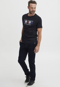 Maglietta nera a maniche corte con strisce orizzontali blu e bianche, caratterizzata dal testo "FQI 924 CLOTHING EST. MCMXIC" sul davanti.