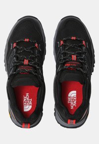 Chaussures de sport noires avec des accents rouges, dotées d'une tige en mesh texturé, de semelles épaisses, d'un embout renforcé et de semelles intérieures de marque.