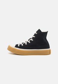 Adidași negri până la glezna, din pânză, cu v�ârf din cauciuc alb, talpă bej și șireturi într-un stil clasic.
