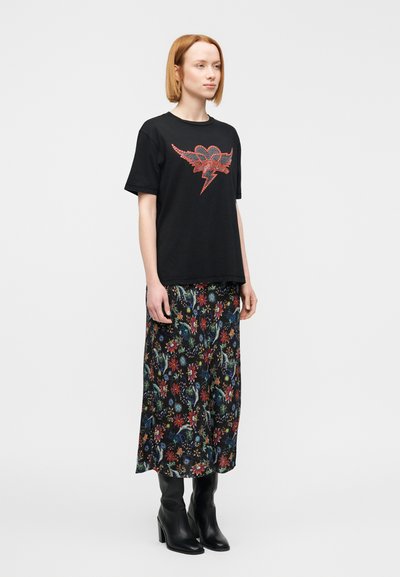 Μαύρο μπλουζάκι με κόκκινη καρδιά και γραφικό κεραυνό, συνδυασμένο με φούστα μακρύ μοτίβο λουλουδιών. Μαύρες μπότες με τακούνι ολοκληρώνουν την εμφάνιση.