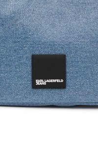 Denim fabric in light blue with a textured surface. Features a black rectangular label with "KARL LAGERFELD JEANS" in white lettering.