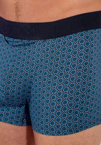 Boxers bleus à motif avec une taille noire arborant le nom de la marque. Le design comprend un motif géométrique en forme de cœur.