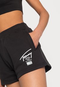 Černé bavlněné šortky s elastickým pasem, přední kapsou a bílým potiskem loga se jmény měst. Měkká textura, ležérní design.