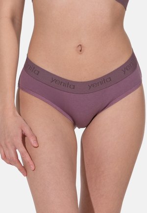 Femme portant un bikini mauve avec une ceinture de marque, montrant le ventre et le haut des cuisses sur un fond blanc.