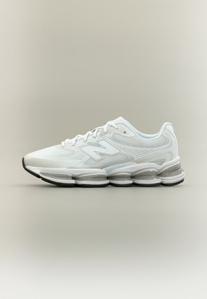 Scarpa da ginnastica bianca con tessuto in rete, chiusura con lacci e suola spessa segmentata progettata per ammortizzazione e supporto.