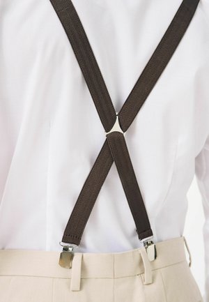 Suspendere maro cu model în zigzag, cu clipsuri argintii, care se intersectează deasupra unei cămăși albe, purtate cu pantaloni bej deschis.
