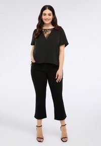 Černé tričko s krátkým rukávem a krajkovým detailem na výstřihu, sladěné s černými zkrácenými kalhotami a černými sandály na podpatku. Hladká tkanina, volný střih.