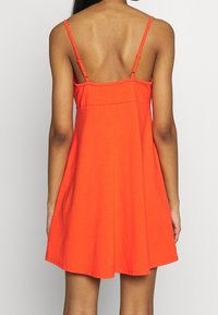 Robe sans manches orange avec un corsage ajusté et une jupe évasée, fabriquée en tissu de coton doux. Fines bretelles avec des caractéristiques ajustables.