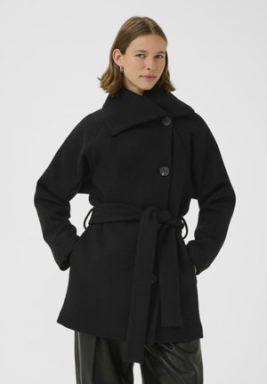 Zwarte wolmix jas met een brede kraag, dubbele knopen, riem en oversized mouwen. Beschikt over een gestructureerde afwerking.