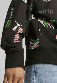 Sudadera negra con estampados gráficos coloridos, que presenta logotipos y diseños en rosa, verde y blanco. Puños y dobladillo acanalados. Material de algodón.