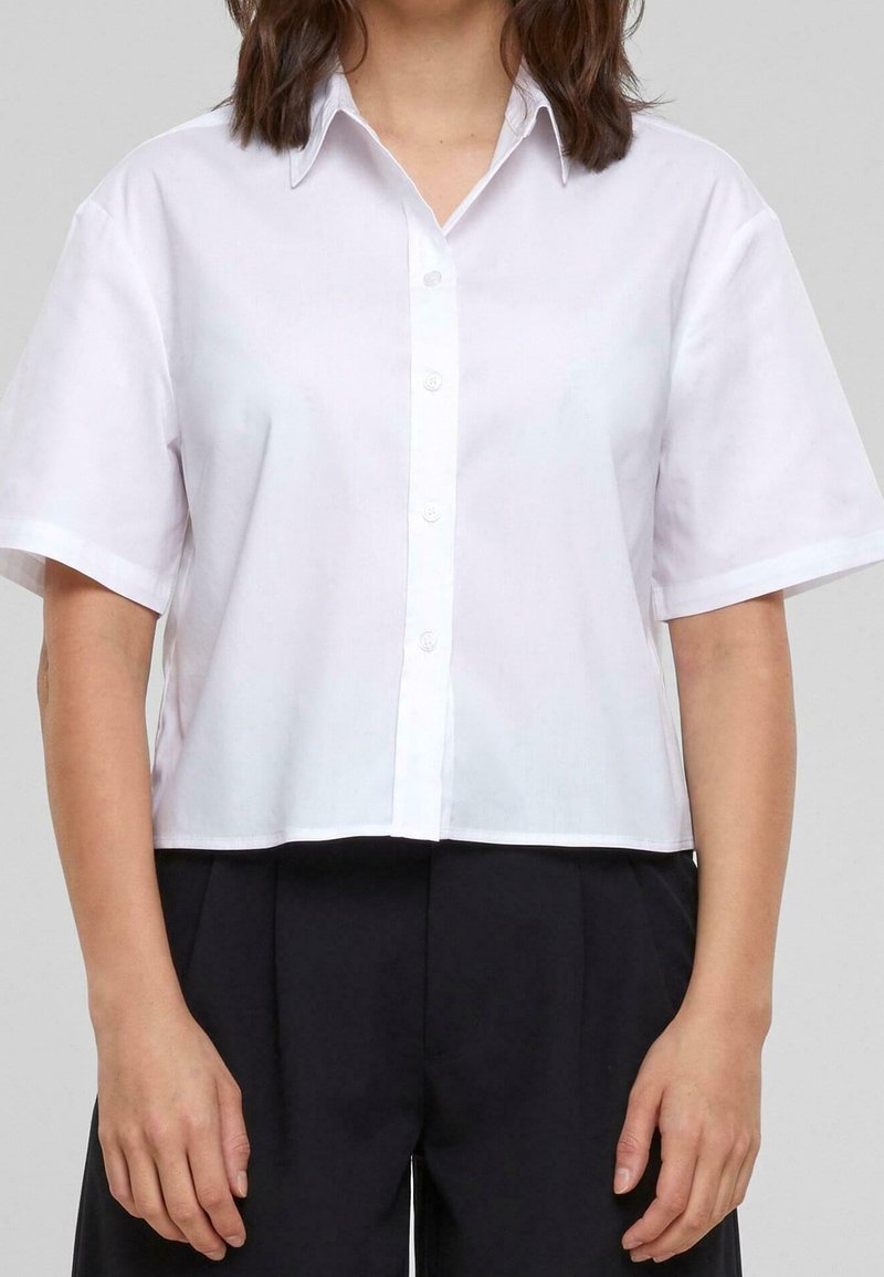 Short-sleeve white button-up shirt, collared, cropped design, smooth cotton fabric, front placket, paired with black high-waisted pants.
