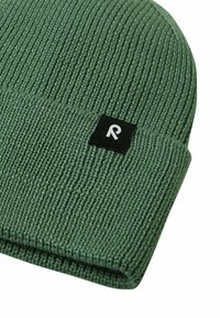 Zielona dzianinowa czapka beanie o prążkowanej teksturze, z czarną metką z białą literą "R". Projekt jest prosty i bez zdobień.