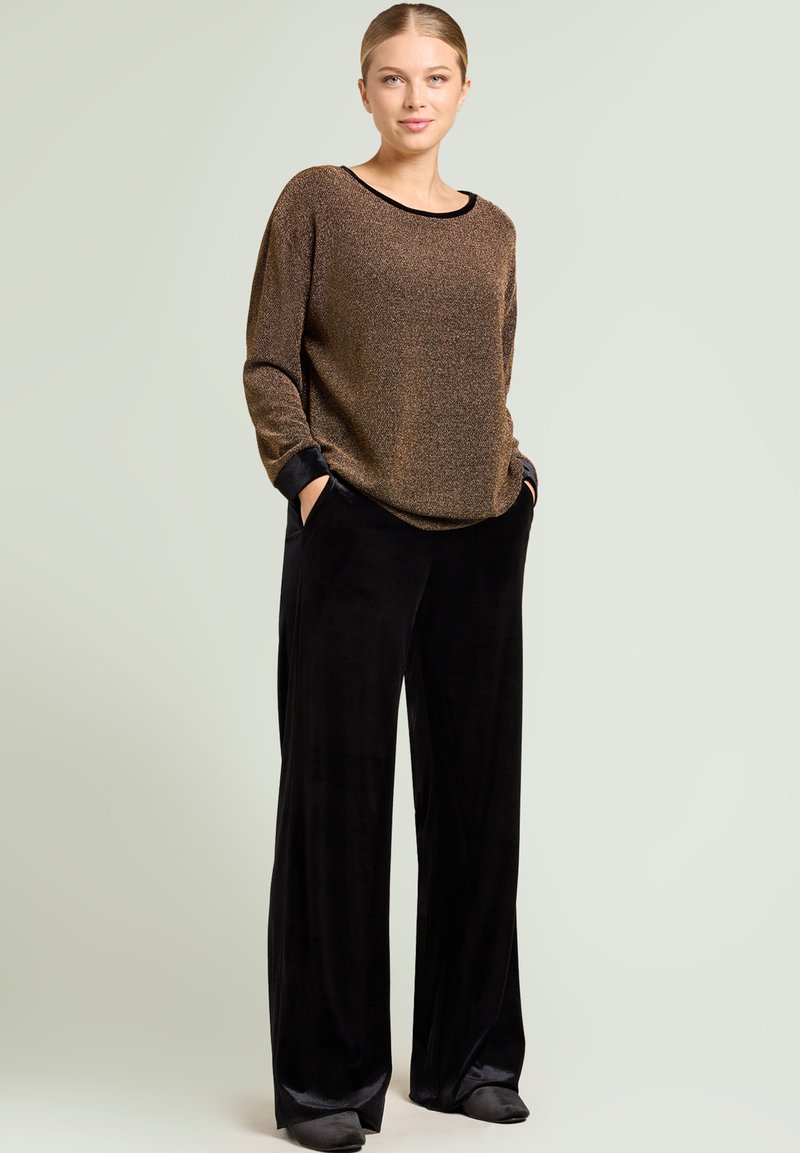 Pull en tricot texturé bronze avec poignets noirs, associé à un pantalon large en velours noir. Les deux pièces présentent des designs décontractés.