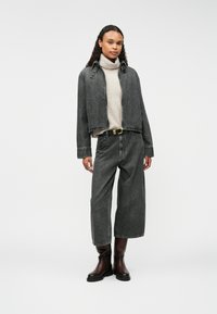 Szara dżinsowa kurtka o skróconym fasonie, w połączeniu z szerokimi szarymi dżinsami. Masywne brązowe skórzane buty i lekki sweter z golfem noszony pod spodem.