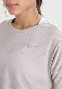 Camiseta deportiva Nike de color rosa claro, hecha de tela transpirable, con una textura de puntos y un pequeño logo plateado en el pecho.
