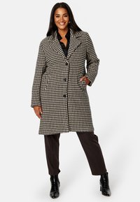 Cappotto a scacchi in bianco e nero, con silhouette aderente, chiusura monopetto e due tasche laterali.