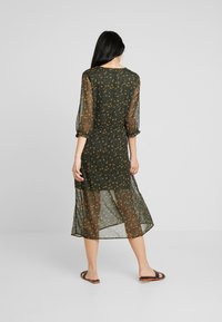 Vestido floral verde oscuro hecho de tela transparente, con mangas abullonadas tres cuartos y cintura fruncida, y una falda transparente de longitud media.