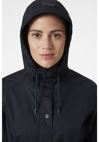 Giacca impermeabile blu navy con cappuccio, caratterizzata da una chiusura con bottoni e cordini regolabili. Tessuto liscio con dettaglio del logo sul cappuccio.