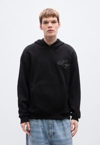 Μαύρο φούτερ με κουκούλα και τσέπη καγκουρό, με αντίθετο κεντημένο λογότυπο "Hugo" στο στήθος. Απαλό ύφασμα, άνετη εφαρμογή, σχέδιο με κουκούλα.