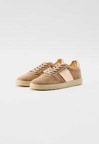Beige semskede sneakers med teksturerte detaljer, rund tå, flat gummisåle og ton-i-ton snøringer. Har et bølgete design på siden.