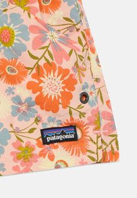 Tecido com padrão floral em tons de rosa, laranja, azul e verde, apresentando uma etiqueta preta da Patagonia e um detalhe em botão.