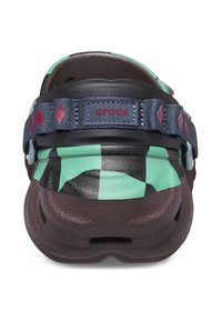 Crocs met een gemêleerd mintgroen en zwart bovenwerk, een bruine onderzool en een marineblauwe verstelbare band met rode accenten en diamanten vormen.