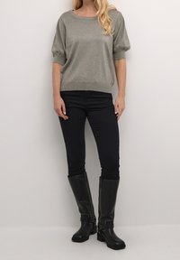 Haut argenté métallique à manches courtes avec un col rond, associé à un pantalon noir ajusté et des bottes noires montantes avec des boucles.