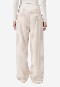 Lichte, high-waisted broek in crème met verticale paarse strepen. Beschikt over een elastische tailleband en een enkele achterzak.