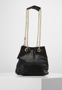 Borsa a secchiello in pelle nera con catene dorate e un manico superiore nero. Presenta due anelli in hardware dorato e una finitura testurizzata.