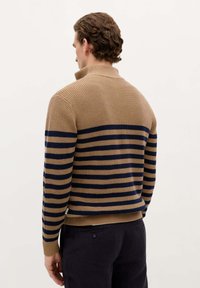 Pull en tricot couleur beige avec des rayures horizontales bleu marine. Il dispose d'un col et de poignets côtelés. Le tissu semble texturé et a une coupe décontractée.