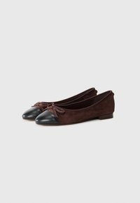 Ballet flats featuring a dark brown suede upper, black leather toe cap, a decorative bow on the front, and a low heel.