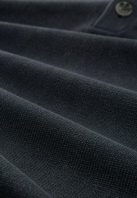 Tessuto blu navy scuro con una tessitura texturizzata, caratterizzato da pieghe e un dettaglio con bottone, che mostra un aspetto liscio e strutturato.