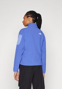 Lagana plava jakna s visokim ovratnikom, teksturiranom tkaninom, kontrastnim plavim zakrpama na laktovima i s logotipom North Face na leđima.