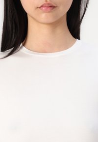 Tricou alb, ajustat, cu decolteu rotund și mâneci scurte, realizat dintr-un material neted și elastic, prezentând un design curat și simplu.