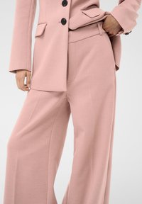 Helles rosa Anzugset mit einem taillierten Blazer mit Revers, Knopfdetails und weiten Hosen mit Taschen. Glatte Textur über das gesamte Outfit.