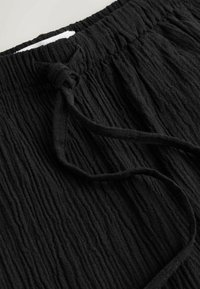 Pantalones de tela negra texturizada con cinturilla elástica y cordón ajustable atado.