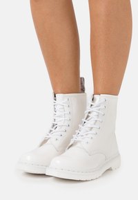 Weiße, glänzende Schnürkampfstiefel mit einer glatten Lederoberfläche, runder Zehenpartie und strukturiertem Gummisohle. Detaillierte Nähte und gepolsterte Knöchel.