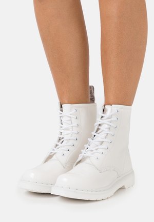 Botas de combate blancas con acabado brillante, cordones y una superficie de cuero suave, con punta redonda y suela de goma texturizada. Costuras detalladas y tobillo acolchado.
