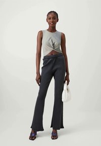 Lysegrønn crop top med vridd frontdesign, kombinert med mørkegrå ribbestrikket fløyelsbukse. Tilbehør inkluderer en hvit håndveske og blå sandaler.