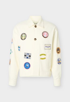 Cremefarvet jakke med knapper, dekoreret med flere farverige broderede patches med tekst og logoer på fronten og ærmerne.