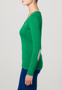Zelený top s dlouhým rukávem z měkkého materiálu. Má výstřih do V, přiléhavý střih a šedé záplaty na loktech. Bez výrazných vzorů nebo kovových doplňků.