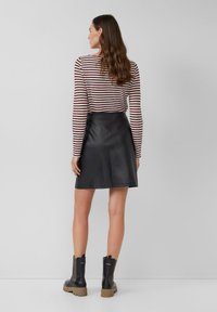 Czarna mini spódniczka z fak leather o sylwetce w kształcie litery A, w połączeniu z bordową i białą paskowaną koszulą z długim rękawem oraz czarnymi botkami za kostkę.