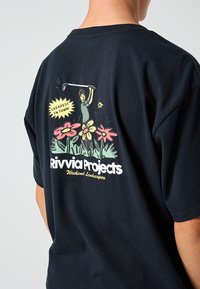 T-shirt preta de algodão com um gráfico colorido nas costas, apresentando flores, um golfista e o texto "Rivvia Projects" e "Mais barato da cidade".