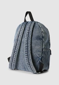 Zaino in denim con una forma arrotondata, cuciture verticali, doppi spallacci imbottiti e un gancio nero. Finitura in tessuto blu chiaro con texture.