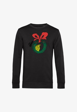 Black sweatshirt featuring a green wreath graphic with a yellow creature and red bow, accented with red berries. Long sleeves and crew neck design.