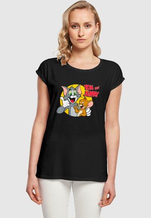Svart t-skjorte med korte ermer som har et fargerikt grafisk bilde av Tom og Jerry, med en rund gul bakgrunn og fet rød tekst.
